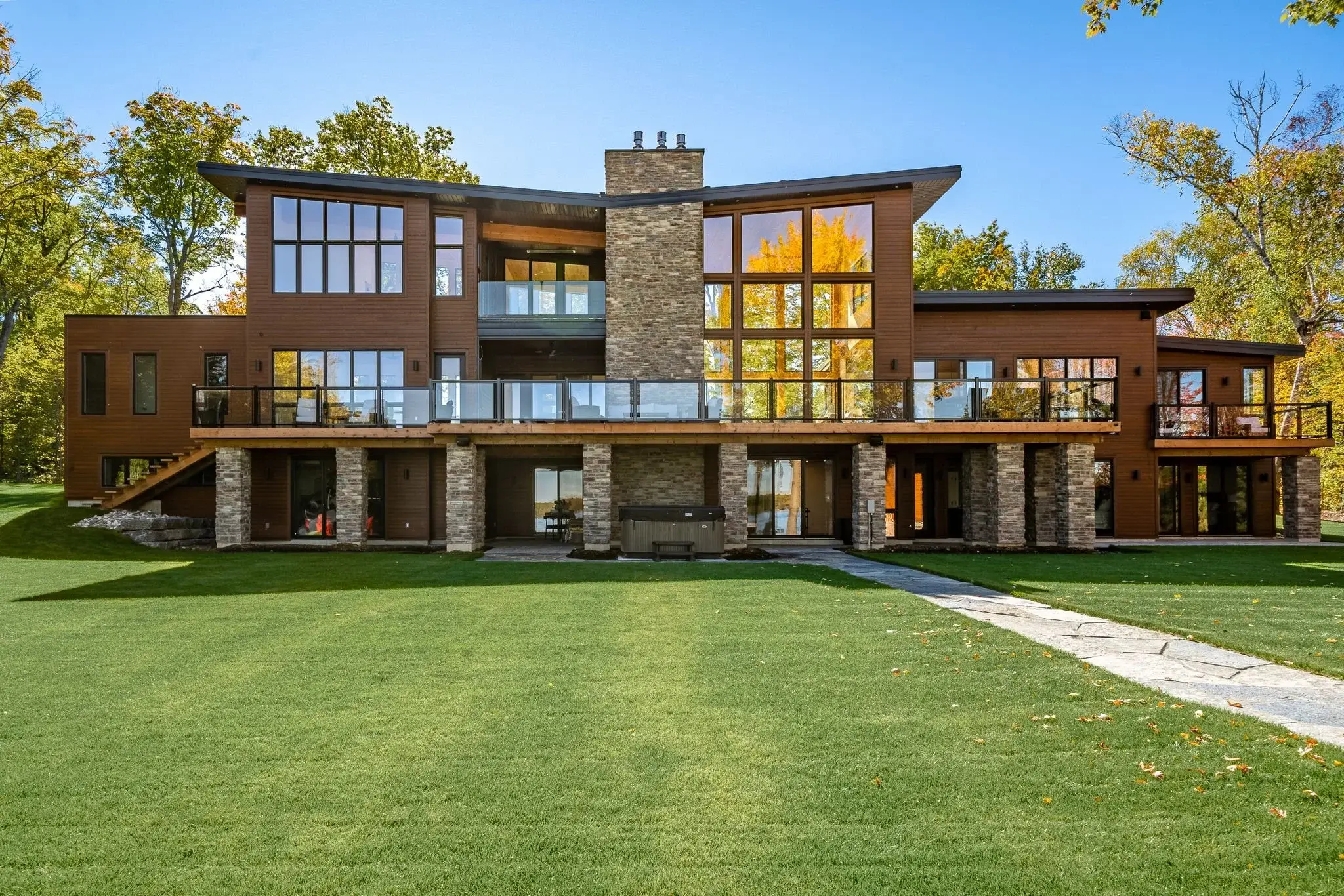 Custom home built by Trademark Homes: warm wood siding, natural stone chimney and floor-to-ceiling windows in autumn light