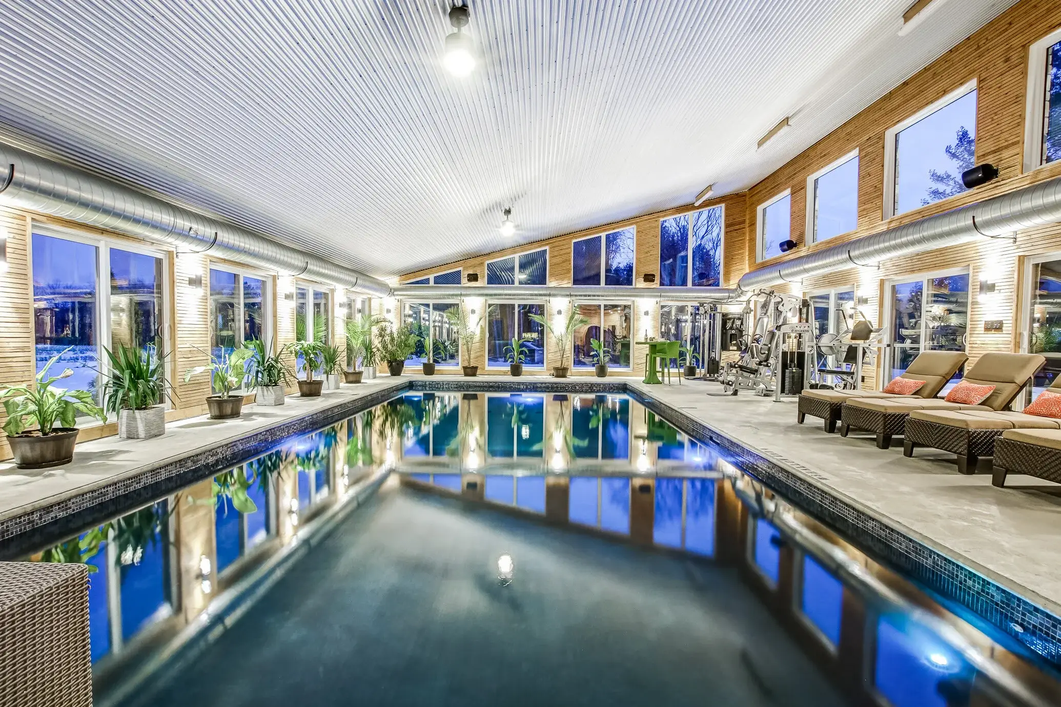 Indoor pool and gym in a Trademark Homes custom build, lit at dusk with floor-to-ceiling windows